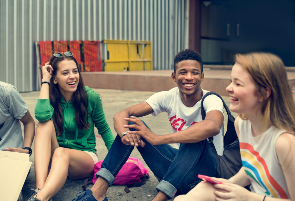 Friends Hipster Teenager Buddies Concept A small group of friends sitting on the ground outside of a building engaged in lively conversation.