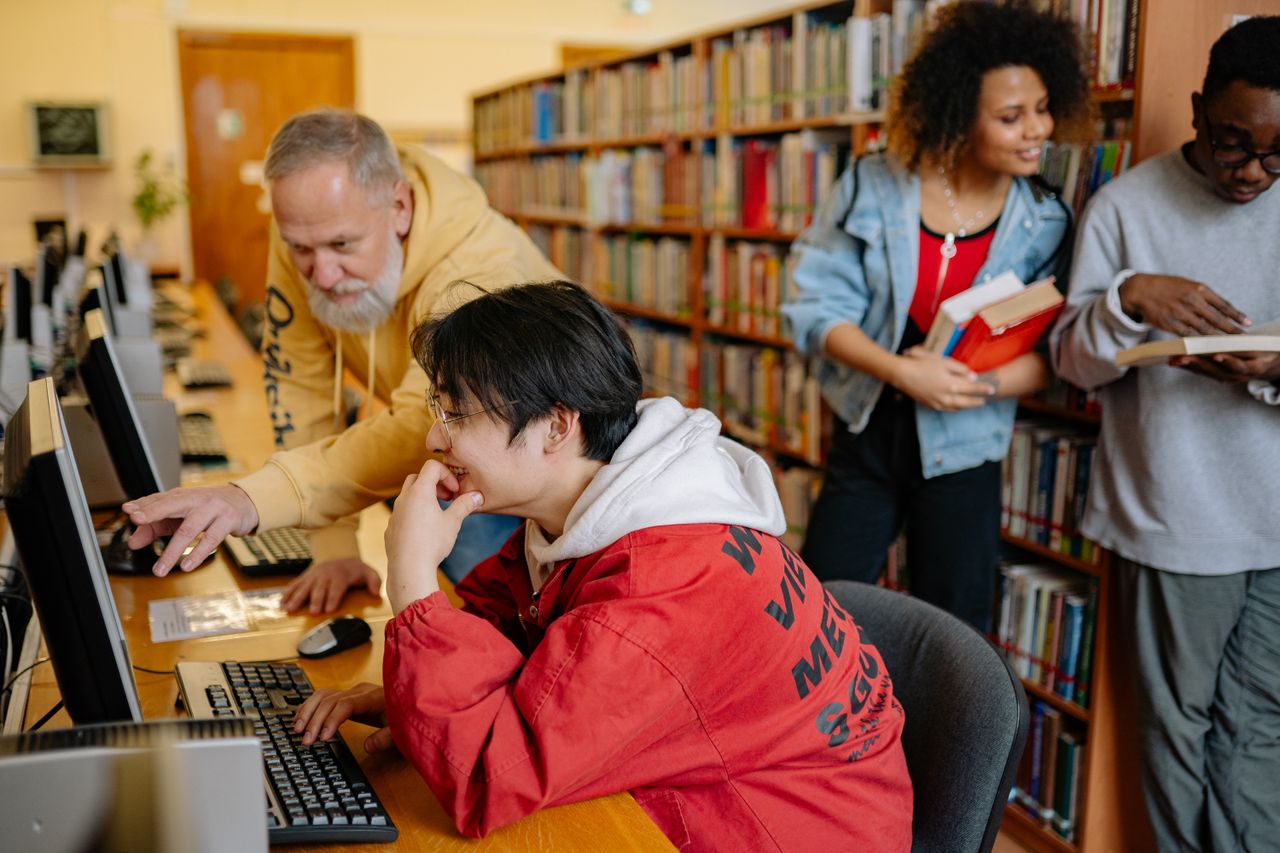 creative-03 Students collaborating and learning in a library setting, engaging with computers and books.