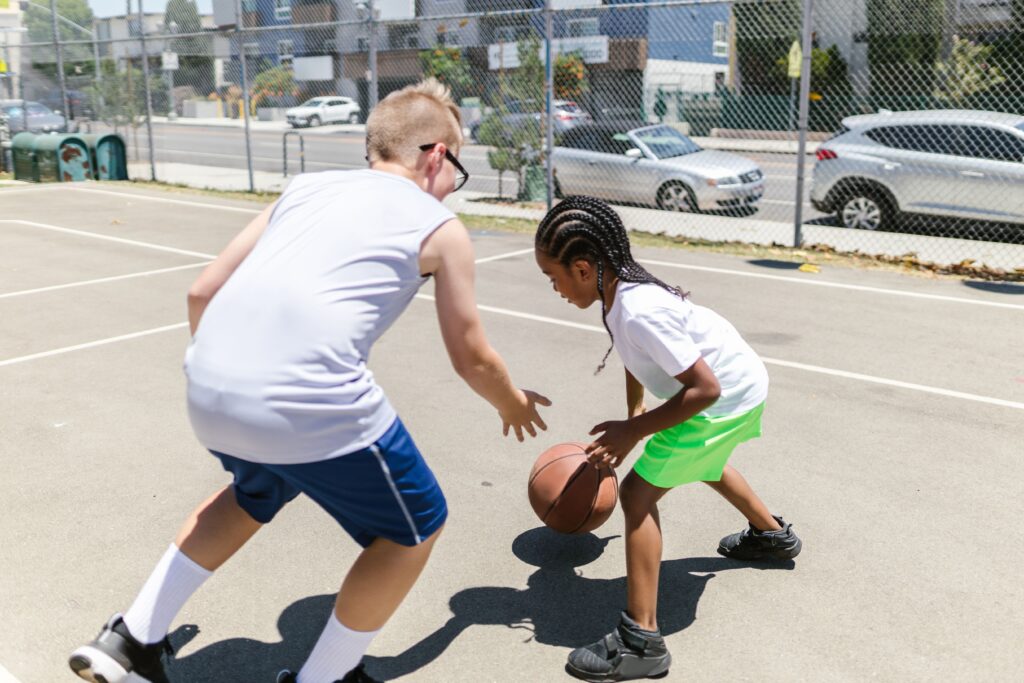 pexels photo 8336980 8336980 Two children playing an energetic game of basketball on an outdoor court during the day.