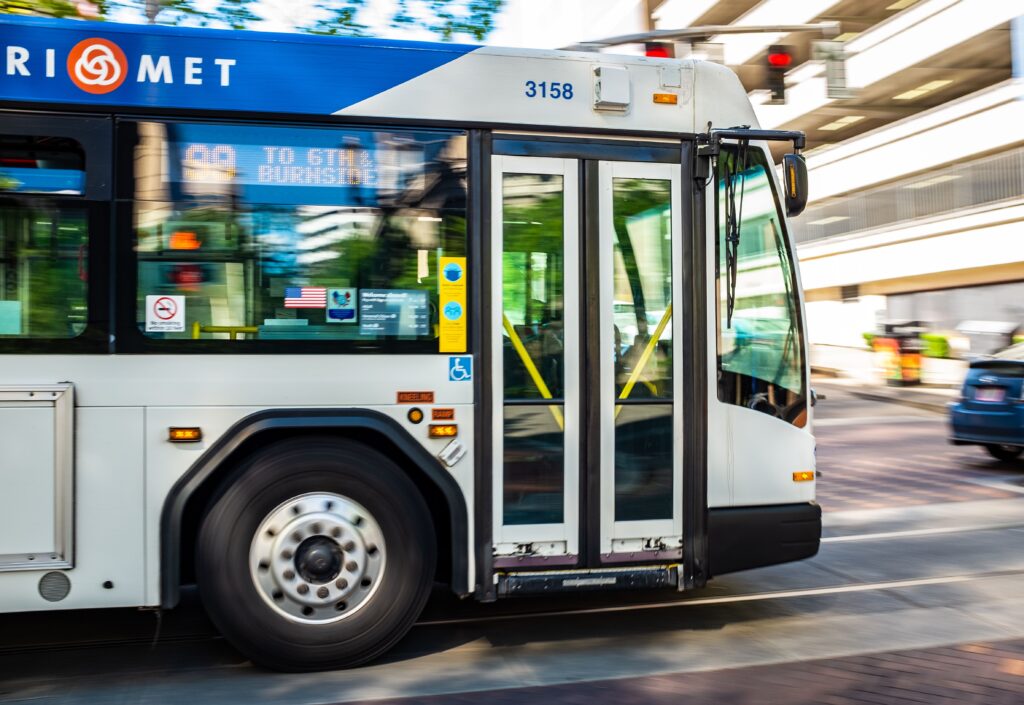 A city bus from TriMet transit system speeds through an urban street during the day.