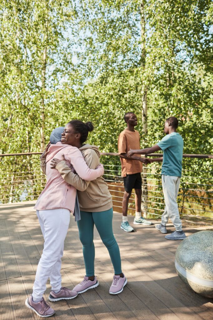 pexels photo 8556492 8556492 A joyful group of friends hugging and chatting outdoors in a sunny park setting, enjoying the summer weather.